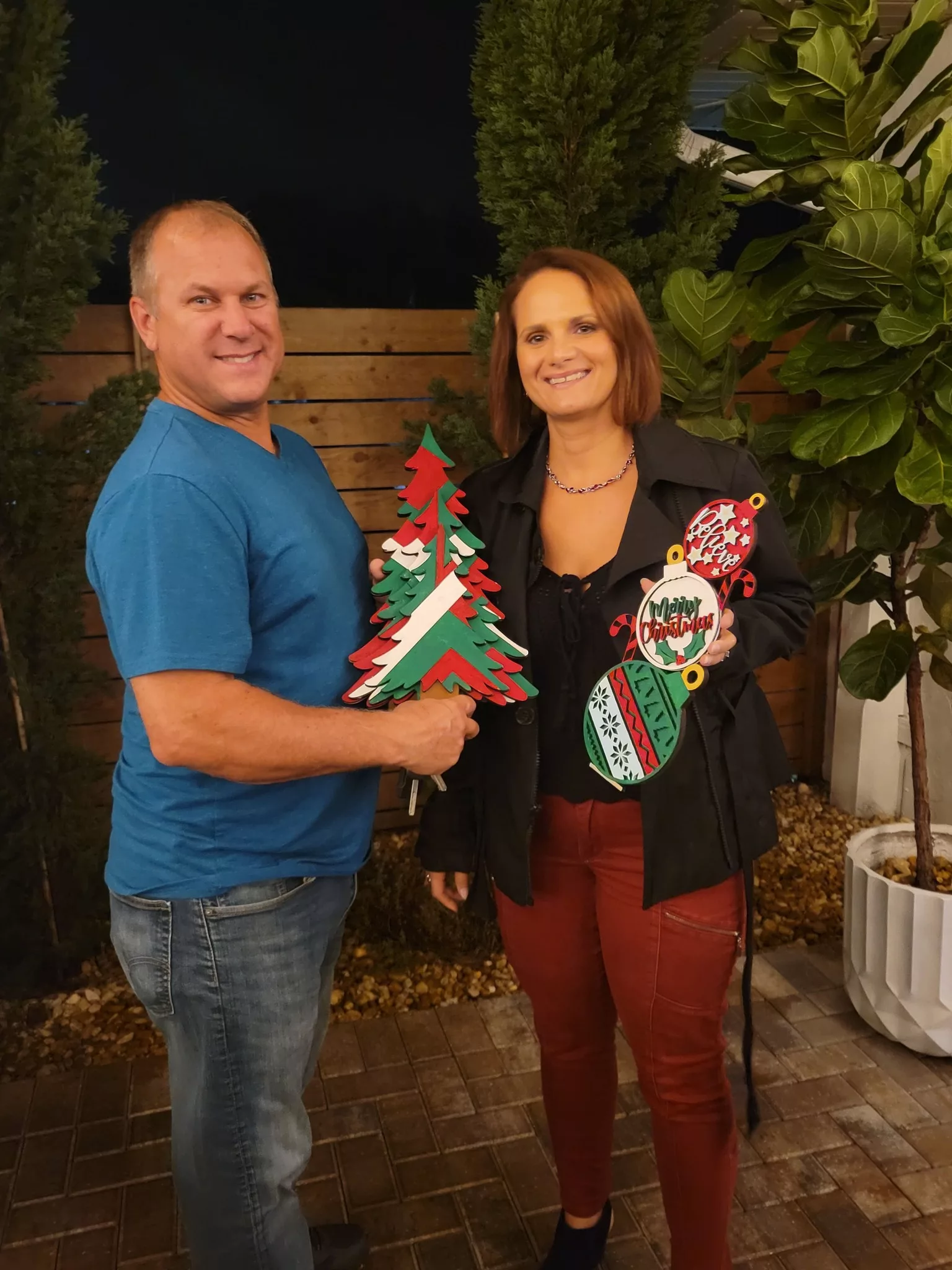A couple smiling with the holiday paintings they made together at a MyMakerScape paint night
