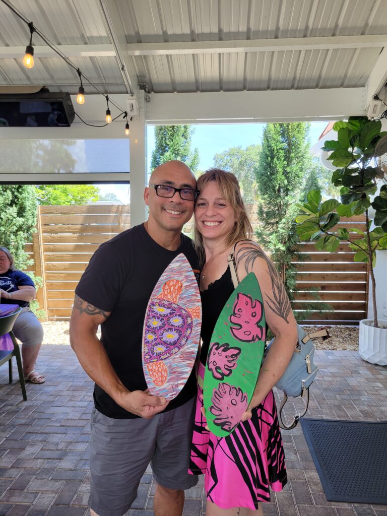 A couple holding the wave boards they painted together at a MyMakerScape workshop